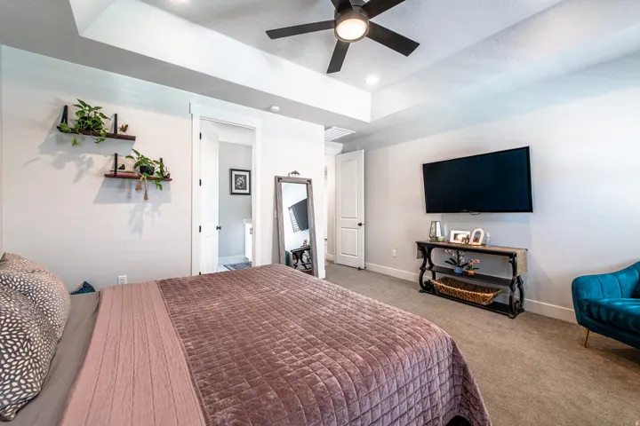 Spacious interior room featuring a tray ceiling with a ceiling fan, light gray wall paint, and light-colored carpet flooring