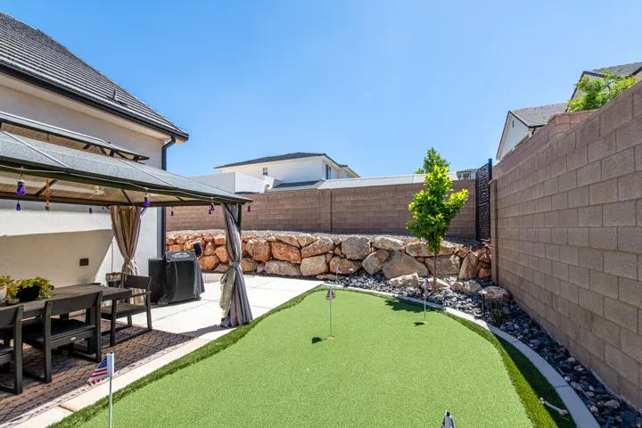 Backyard featuring a covered patio, artificial turf putting green, concrete paver patio, and natural rock landscaping