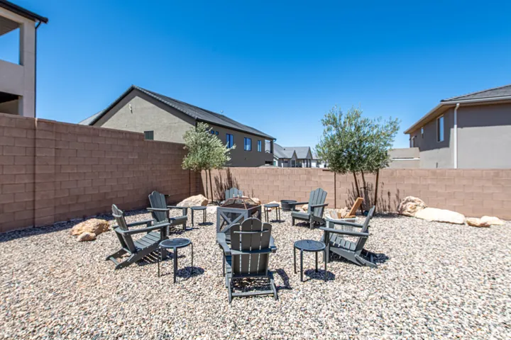 Gravel backyard featuring a built-in fire pit, multiple Adirondack chairs, two mature trees, and a block privacy wall