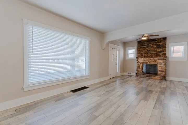 Spacious living area featuring light wood-finish flooring, a stone fireplace, and a ceiling fan