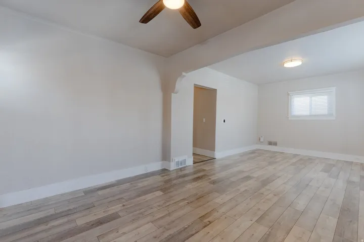 Spacious room featuring wood-finish flooring, light-toned walls, and a ceiling fan with integrated lighting