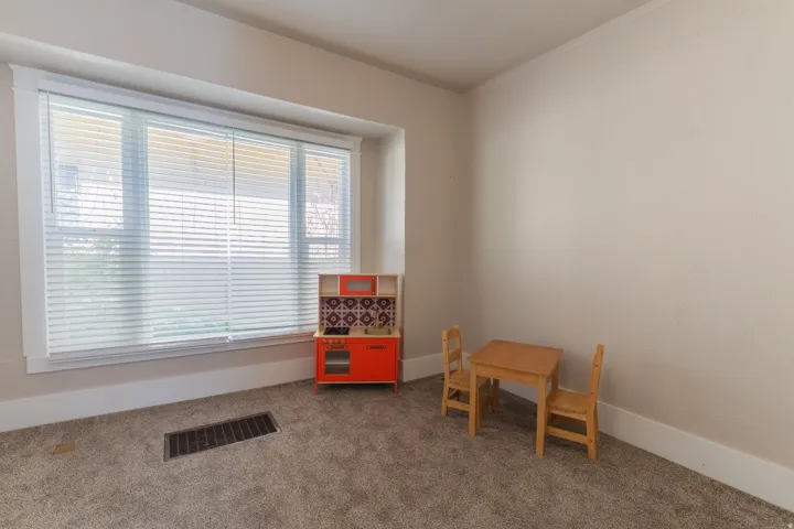 Room featuring a large window with white blinds, neutral-toned walls, and carpeted flooring