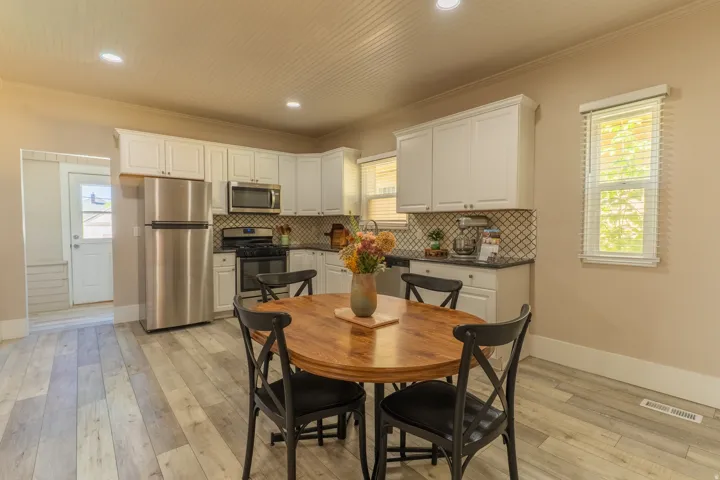 Kitchen area featuring white cabinetry, stainless steel appliances, a geometric tile backsplash, dark countertops, and wood-finish flooring