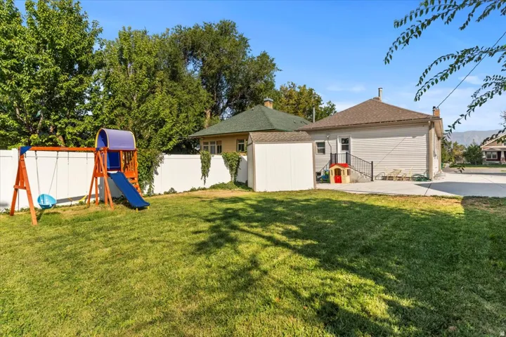 Expansive backyard featuring a lush lawn, white privacy fencing, mature trees, a concrete patio, and a dedicated storage shed