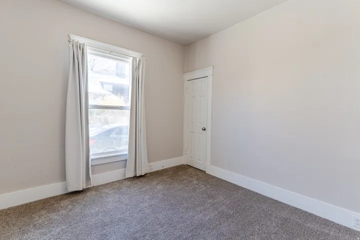 Room featuring neutral painted walls, white trim, gray carpeting, a window with white casing, and a white paneled door