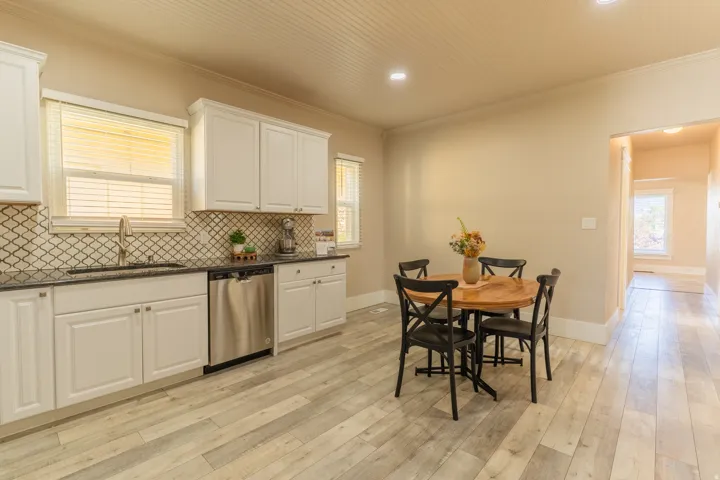 Kitchen featuring white cabinetry, dark countertops, a decorative tile backsplash, stainless steel dishwasher, and wood-finish flooring