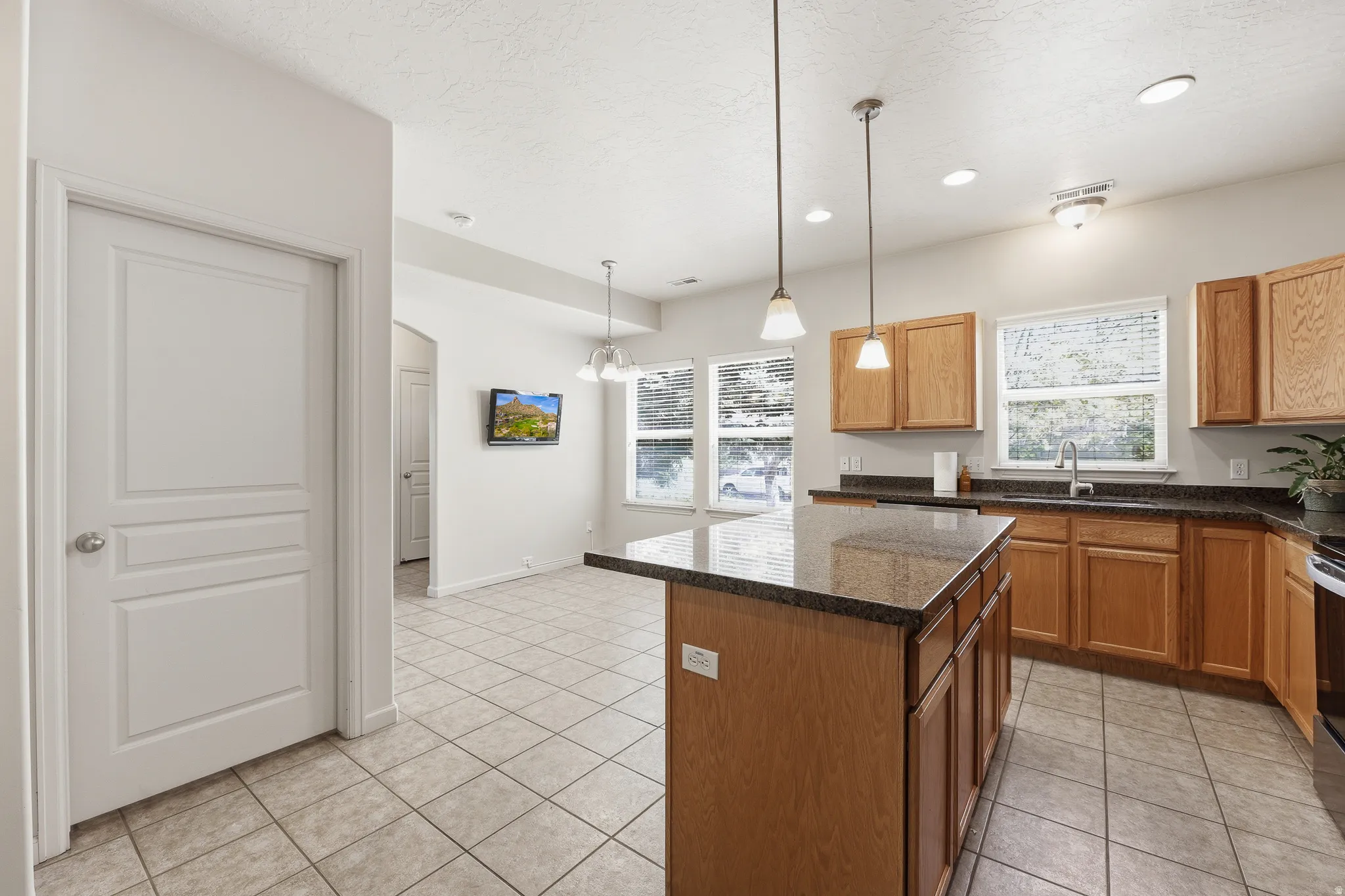 Kitchen featuring a center island with pendant lighting, light wood cabinetry, dark countertops, and tile flooring