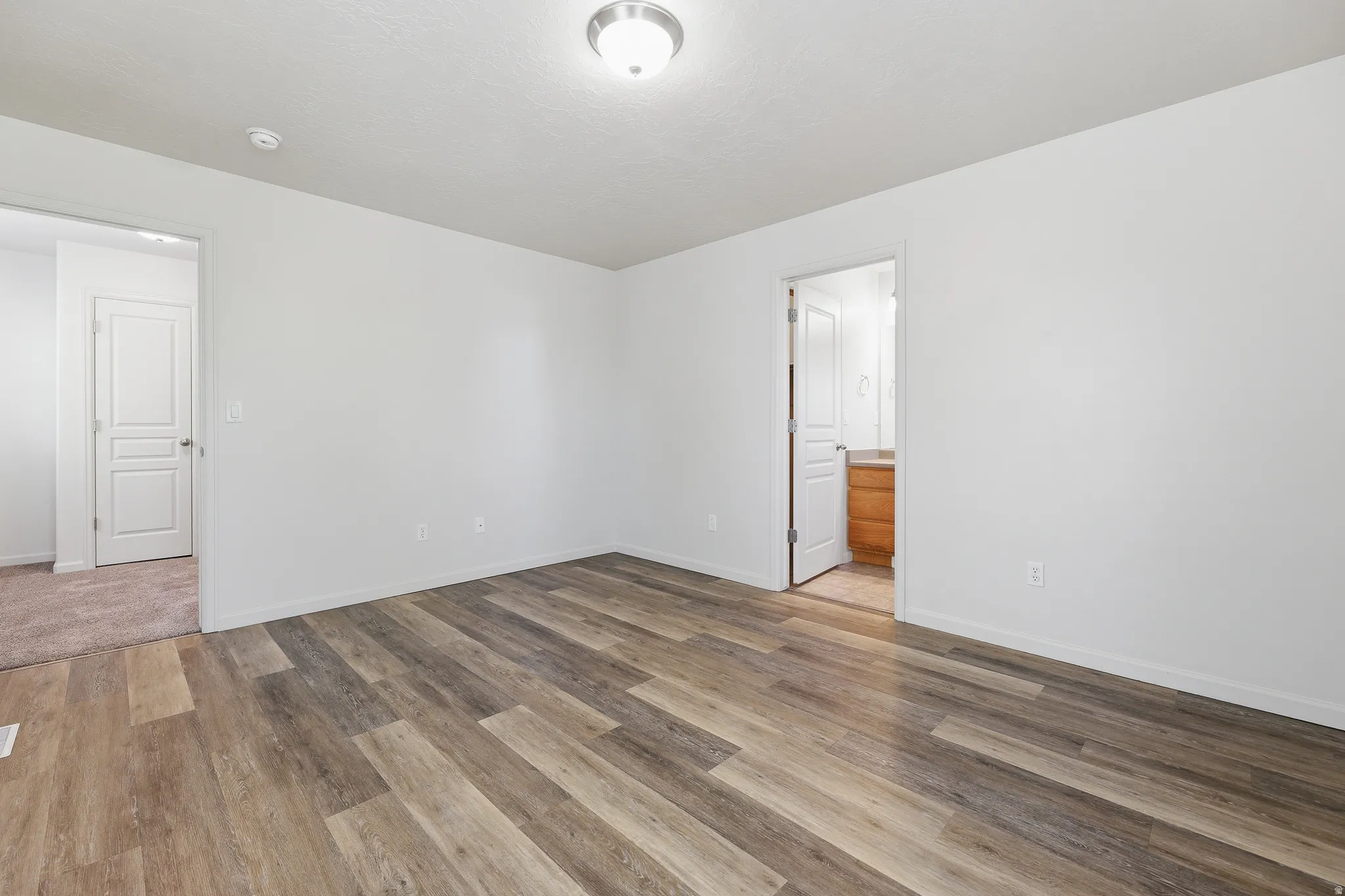 Bright room featuring multi-toned wood-finish flooring and crisp white walls