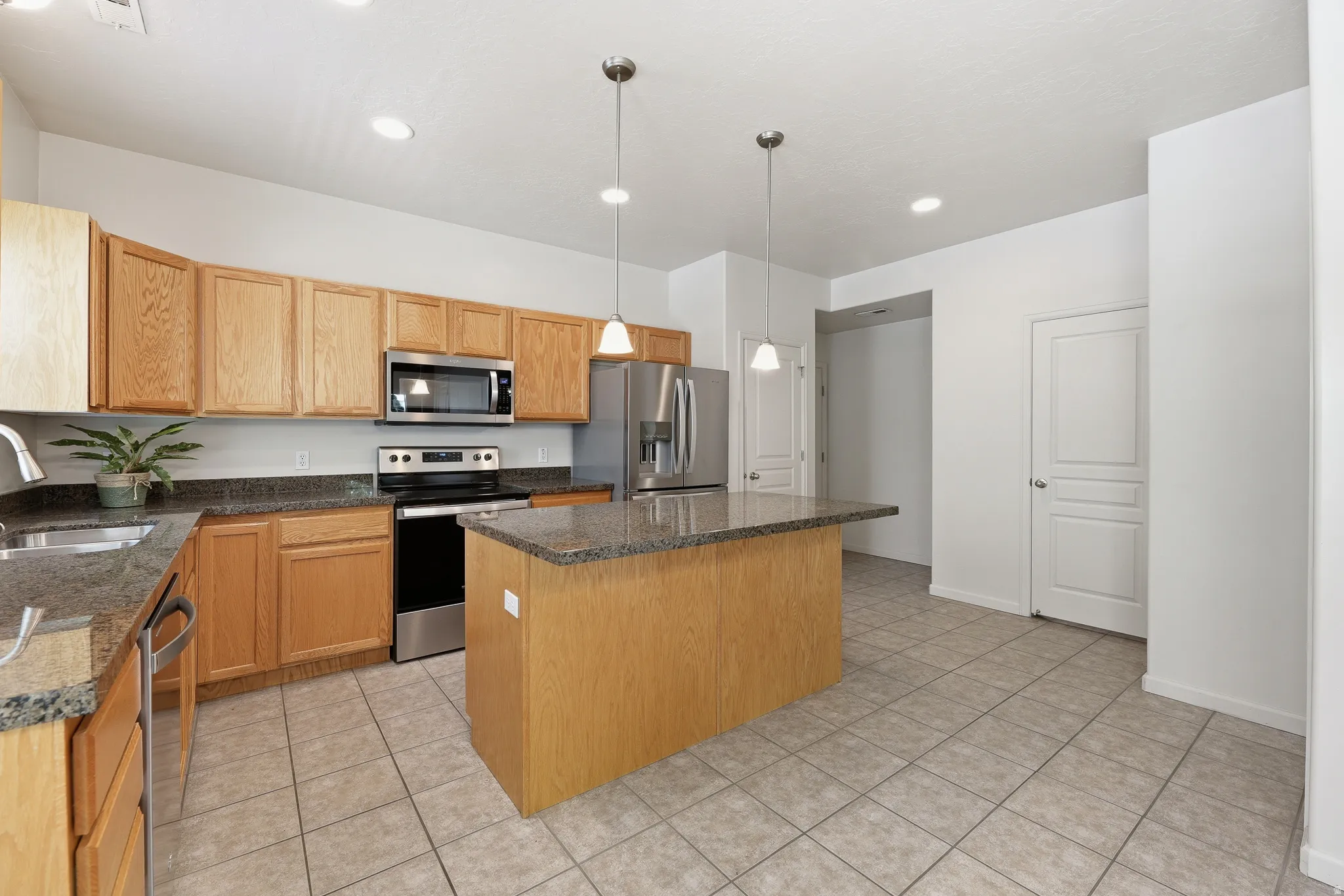 Kitchen featuring a central island with a stone countertop, light wood cabinetry, stainless steel appliances, tile flooring, and recessed lighting