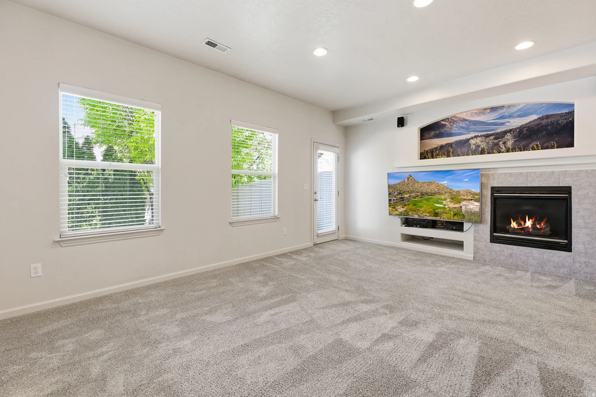 Living area featuring light gray carpeting, a fireplace with a tiled surround, recessed lighting, and an exterior door