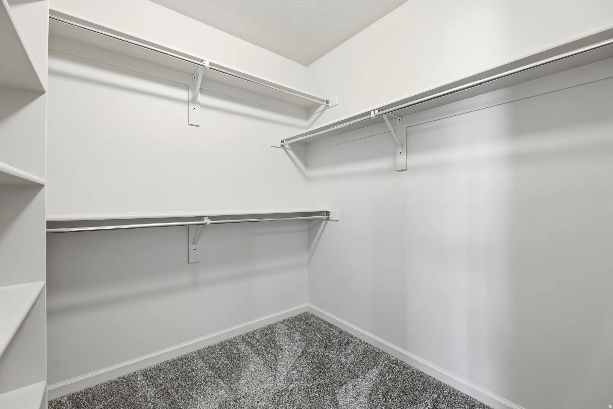 Walk-in closet featuring built-in shelving, multiple hanging rods, white walls, white trim, and patterned grey carpeting