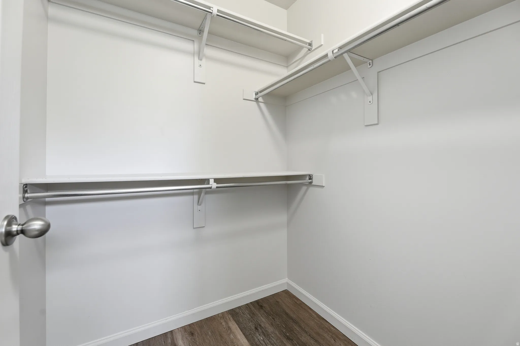 Walk-in closet featuring white shelving, chrome hanging rods, and wood-finish flooring