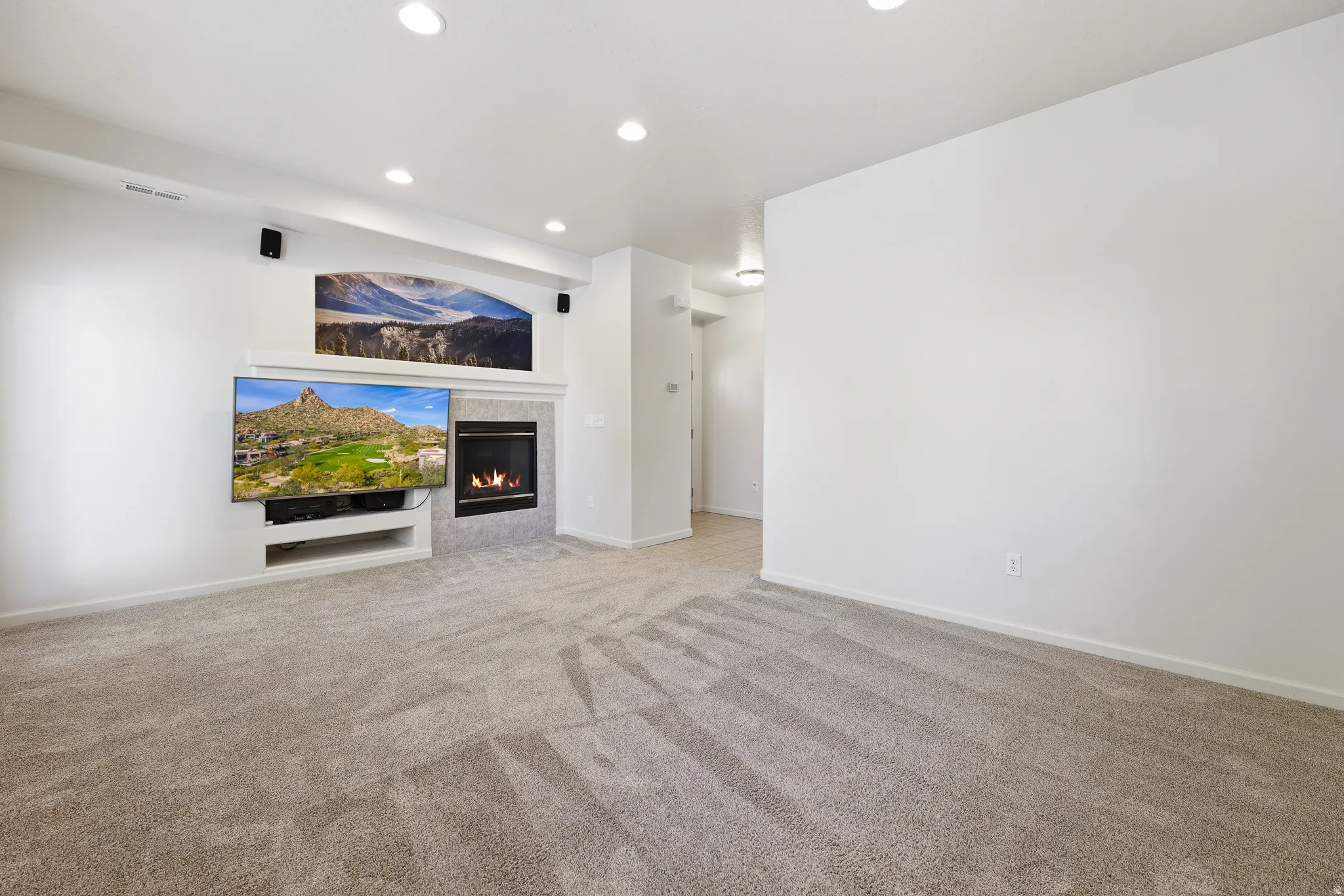 Spacious room featuring plush gray carpeting, recessed ceiling lighting, a built-in media center, and a tiled fireplace
