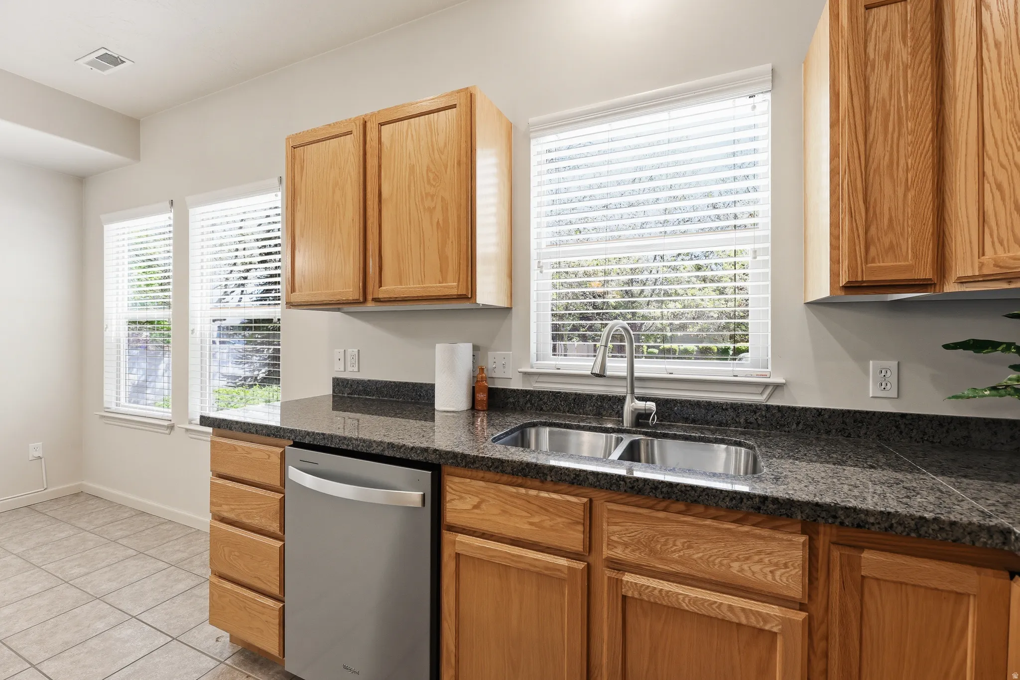 Kitchen featuring wood cabinetry, dark speckled countertops, stainless steel undermount sink with a gooseneck faucet, and a stainless steel dishwasher