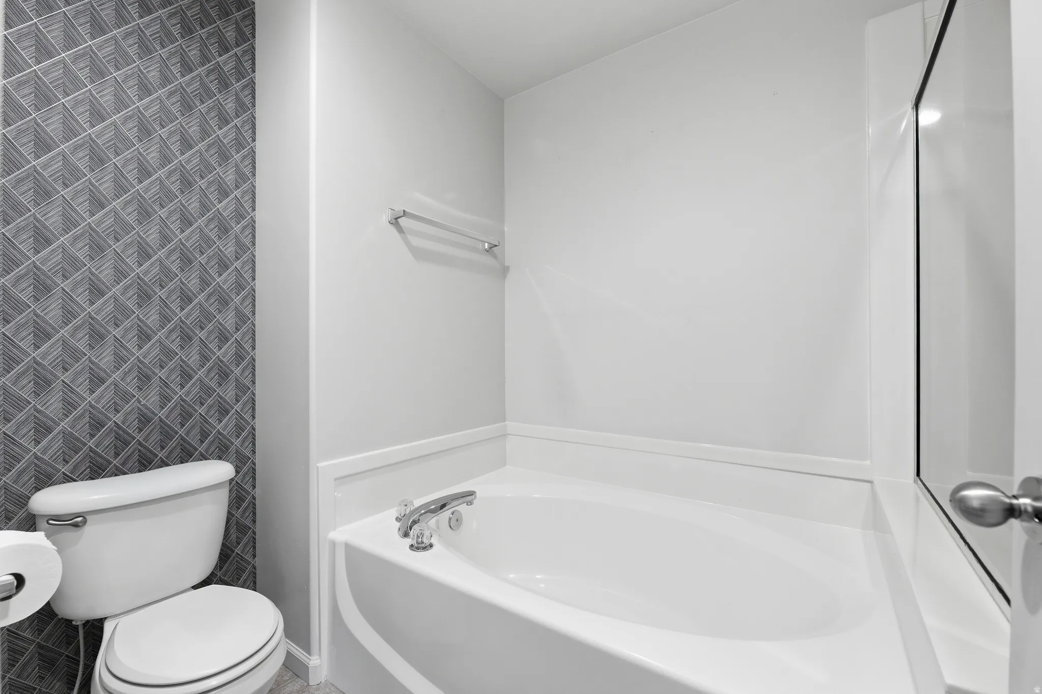 White soaking tub with chrome fixtures, complemented by a patterned accent wall and white toilet