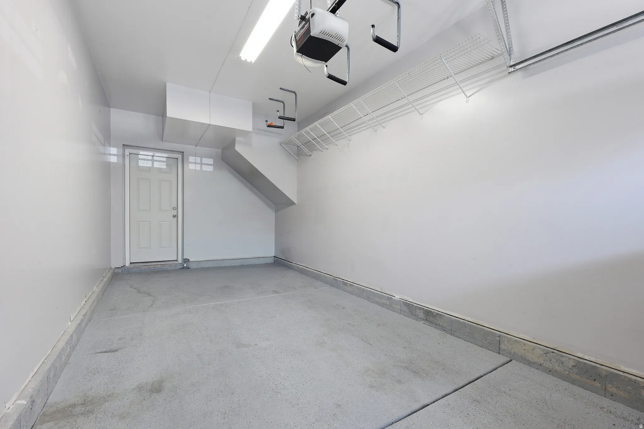 Spacious garage featuring a concrete floor, overhead fluorescent lighting, and a white paneled door