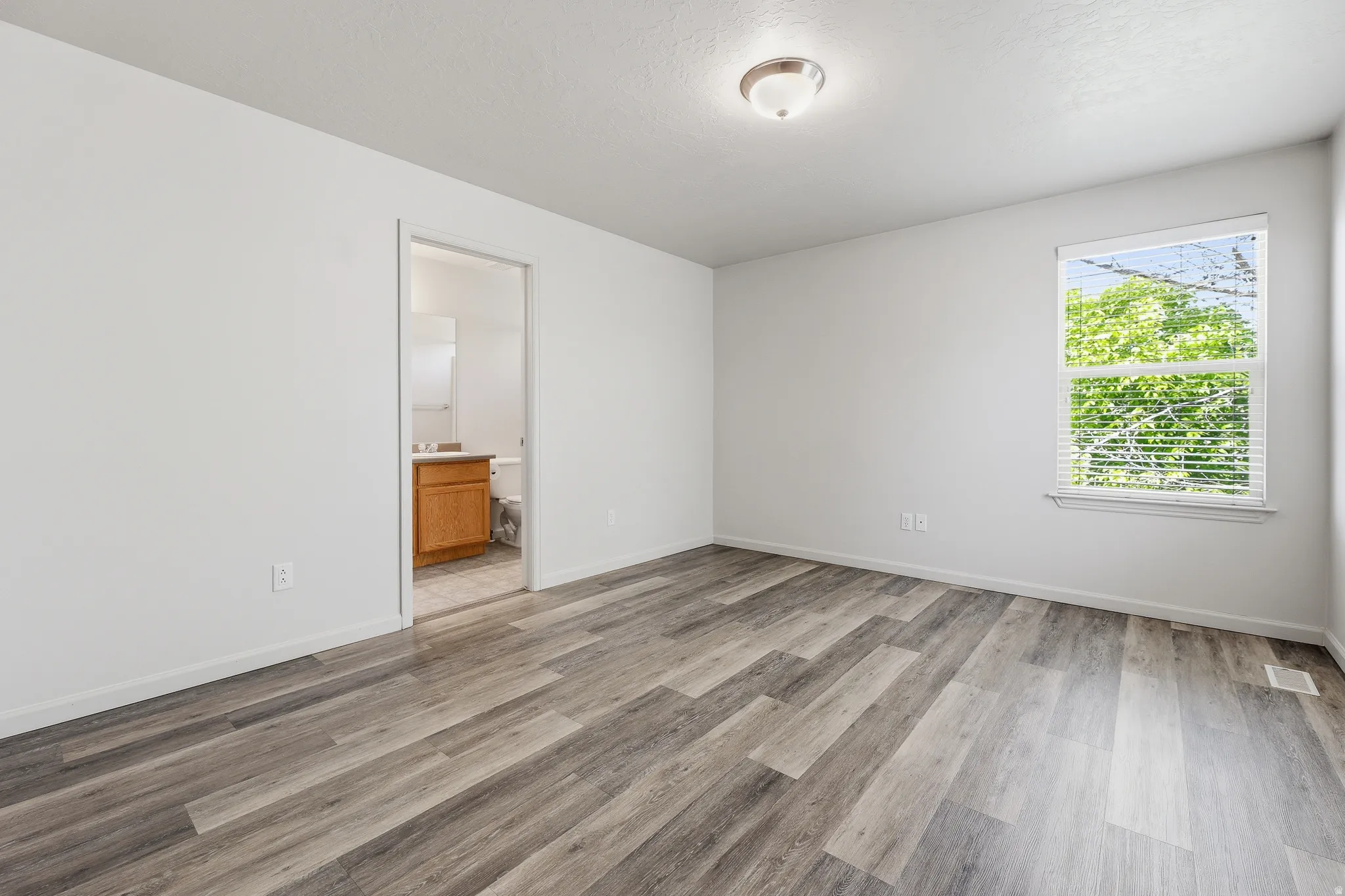 Spacious room featuring wood-finish flooring, white walls, and a window with blinds