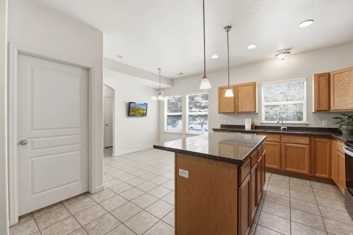 Kitchen featuring a center island with pendant lighting, light wood cabinetry, dark countertops, and tile flooring