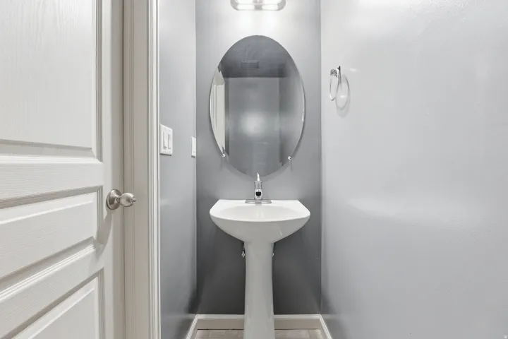 Pedestal sink with an oval mirror and overhead light fixture