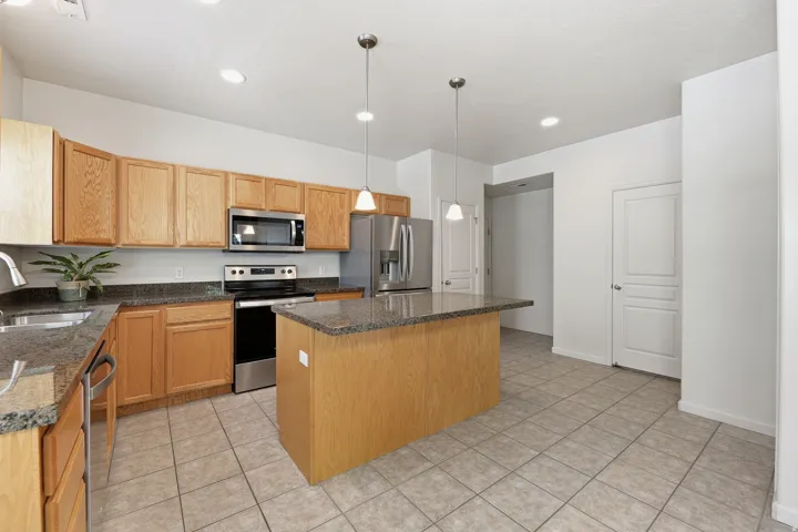 Kitchen featuring a central island with a stone countertop, light wood cabinetry, stainless steel appliances, tile flooring, and recessed lighting