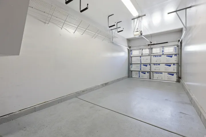 Garage featuring concrete flooring, overhead wire shelving, wall-mounted utility hooks, and an insulated garage door with window inserts