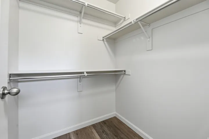Walk-in closet featuring white shelving, chrome hanging rods, and wood-finish flooring