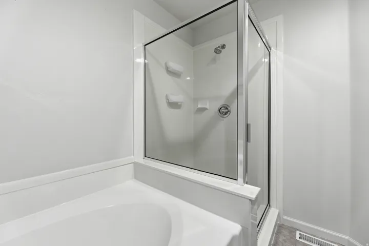 Bathroom featuring a glass-enclosed shower with a chrome showerhead and control, white wall surround, and an integrated bathtub