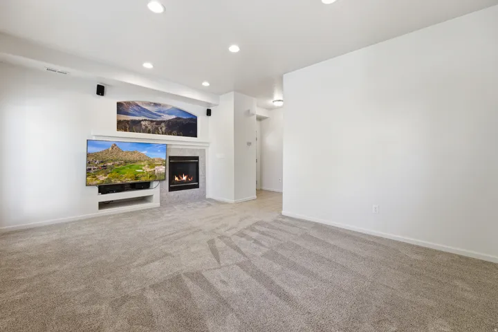 Spacious room featuring plush gray carpeting, recessed ceiling lighting, a built-in media center, and a tiled fireplace