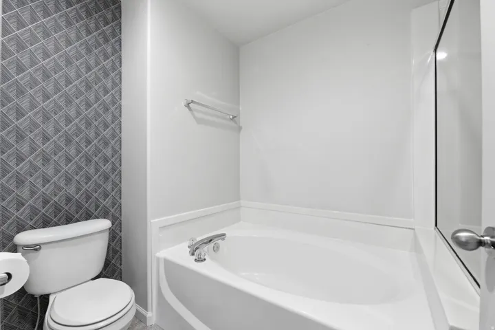 White soaking tub with chrome fixtures, complemented by a patterned accent wall and white toilet
