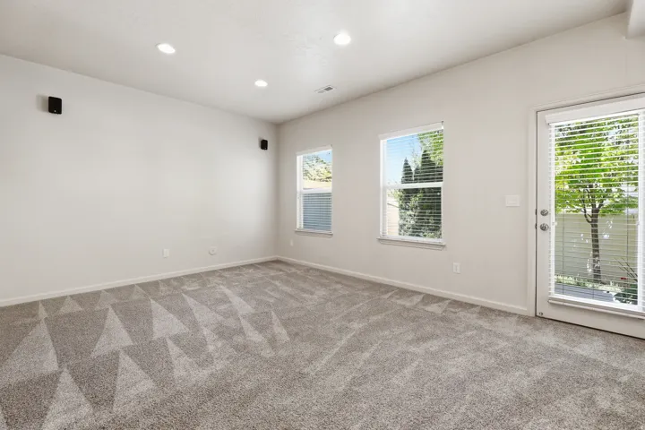 Spacious room featuring neutral carpeting with a geometric pattern, recessed lighting, and wall-mounted speakers