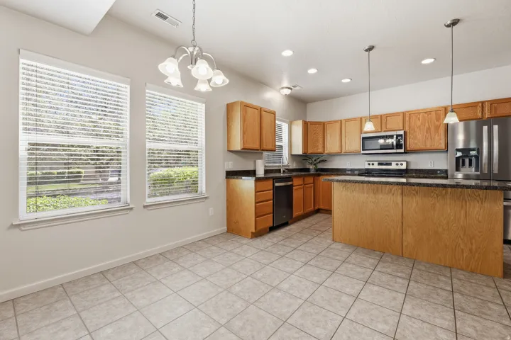 Kitchen featuring wood cabinetry, stone countertops, stainless steel appliances, and a central island