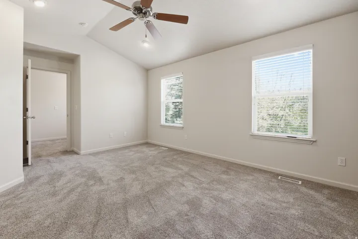 Spacious room featuring vaulted ceilings, recessed lighting, a ceiling fan with wood-finish blades, soft grey carpeting, and two windows with blinds