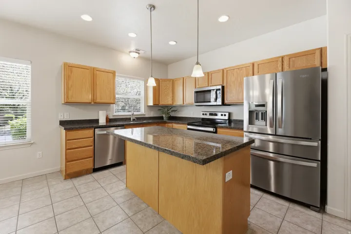 Kitchen featuring a central island with a stone-finish countertop, stainless steel appliances, tile flooring, and ample cabinetry