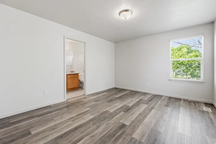 Spacious room featuring wood-finish flooring, white walls, and a window with blinds