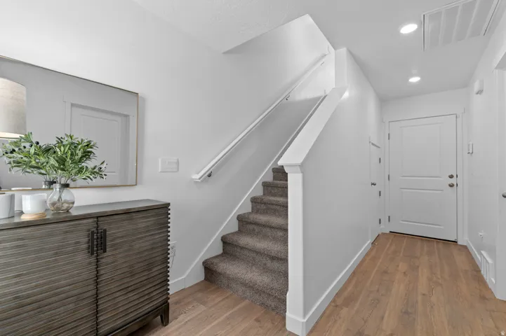 Entryway featuring wood-finish flooring, white trim, and a carpeted staircase with a white handrail