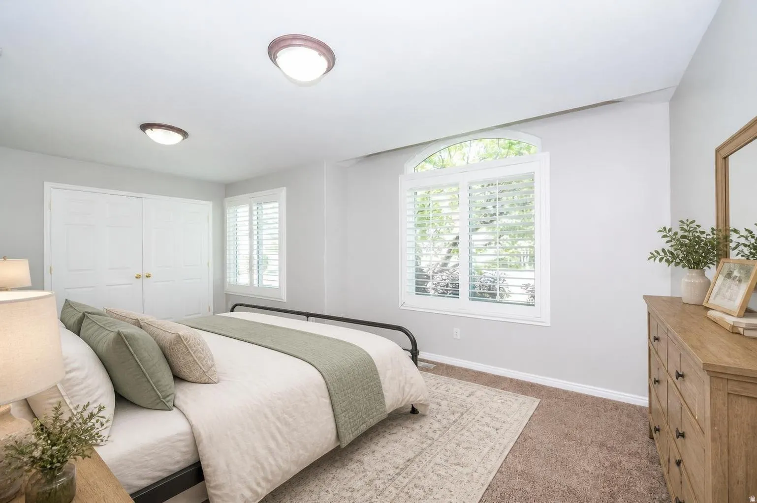Arched window with plantation shutters, twin-door closet, ceiling-mounted light fixtures, and carpeted flooring