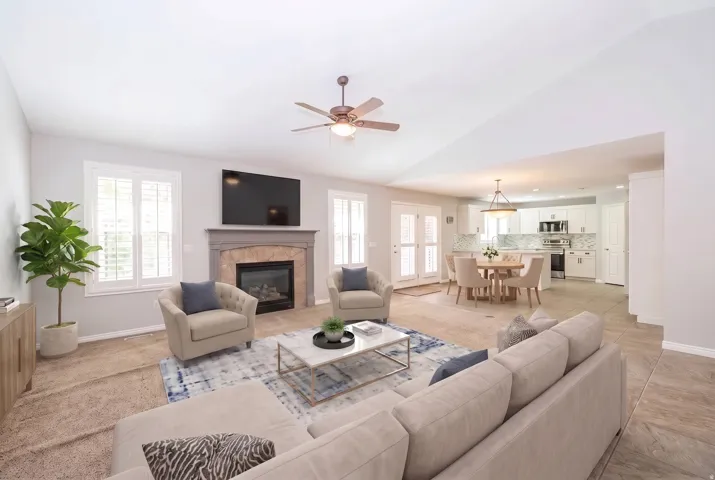 Vaulted ceiling with a ceiling fan, fireplace with stone surround, white shuttered windows, French doors, and tile flooring