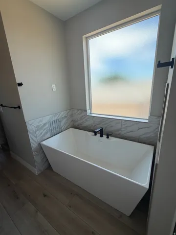 Freestanding rectangular soaking tub with matte black fixtures, set against a tiled accent wall featuring marble-look and mosaic tiles