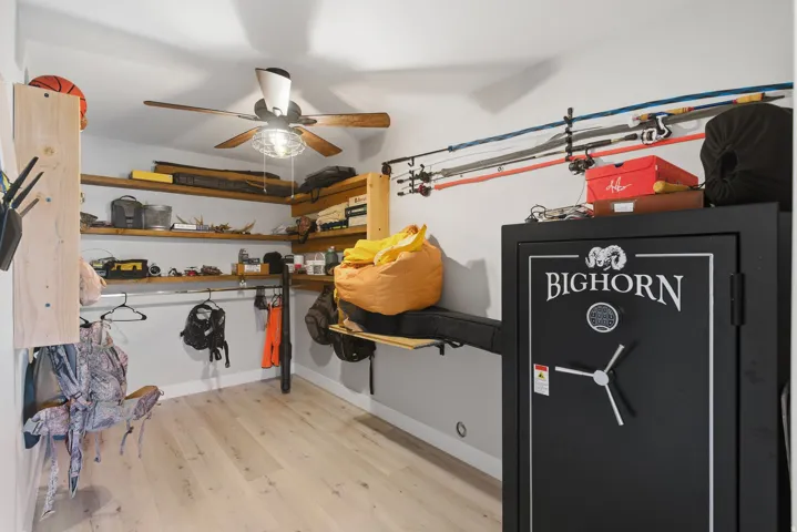 Dedicated storage space featuring light wood-finish flooring, ample built-in wood shelving, and a ceiling fan with light fixture