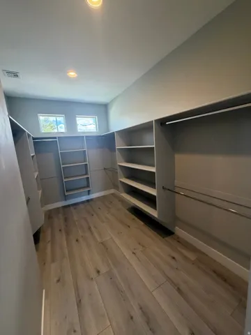 Spacious walk-in closet featuring extensive built-in shelving, hanging rods, wood-finish flooring, recessed lighting, and upper windows