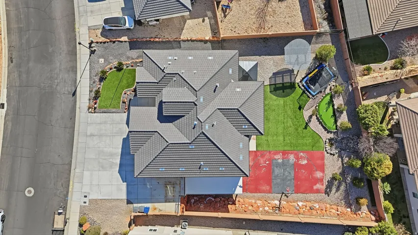 Spacious residential property featuring a multi-gabled roof, extensive concrete driveway, front yard with manicured lawn, rear yard with artificial turf, and a red-painted sports court