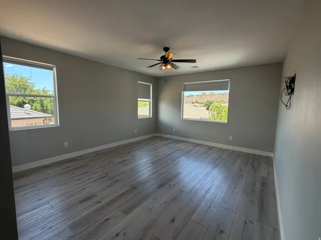 Spacious room featuring wood-finish flooring, light grey walls, and a ceiling fan with integrated lighting