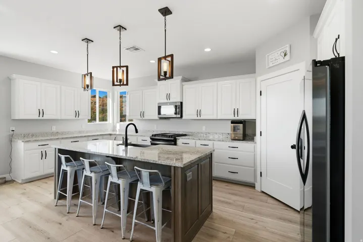 Open-concept kitchen featuring an oversized island with seating, white shaker cabinetry, speckled countertops, and wood-finish flooring