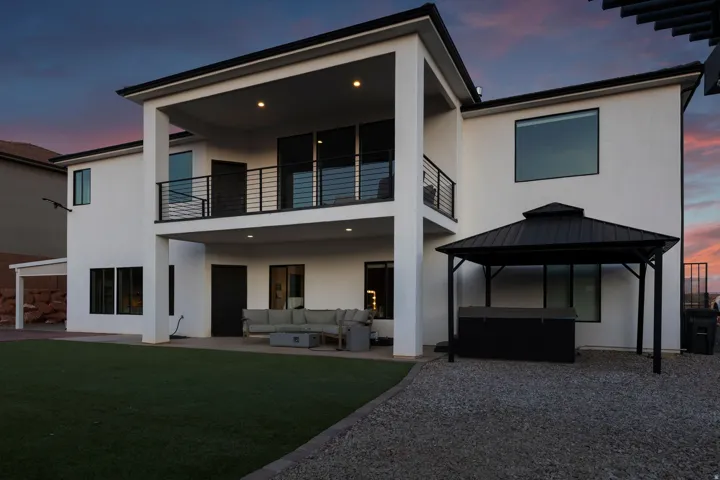 Modern white stucco exterior with a covered patio, second-story balcony with black railings, and a detached black metal gazebo