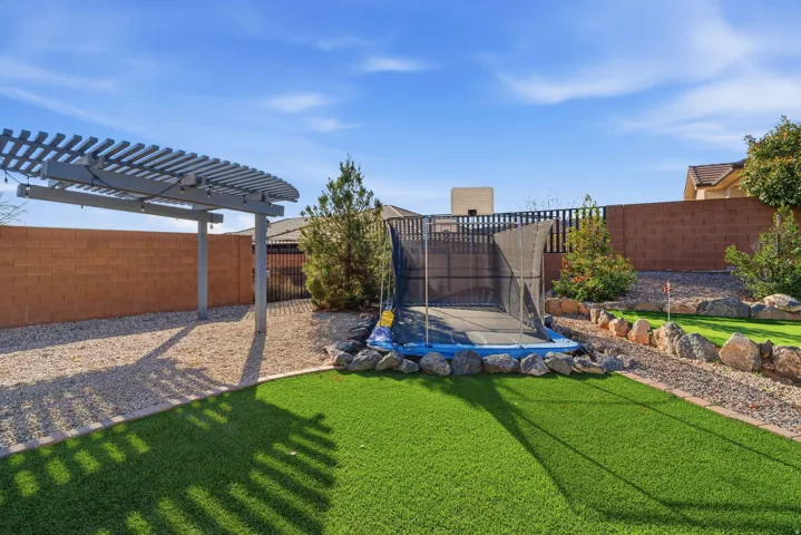 Expansive outdoor space featuring artificial turf, a rock-lined landscaping bed, and a built-in pergola structure