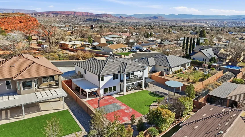 Two-story white exterior with a dark tile roof, featuring a covered patio, upper balcony, and a red-surfaced sport court