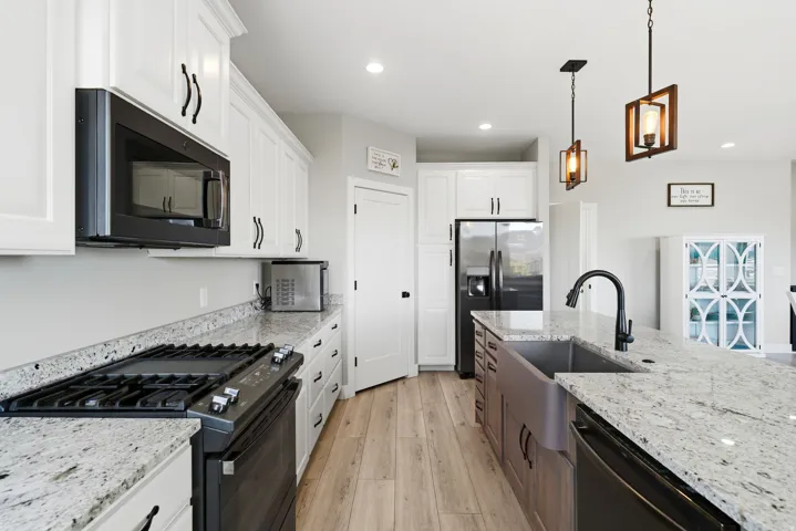 Modern kitchen featuring white cabinetry, granite countertops, wood-finish flooring, a stainless steel refrigerator, and a farmhouse-style sink with a matte black faucet