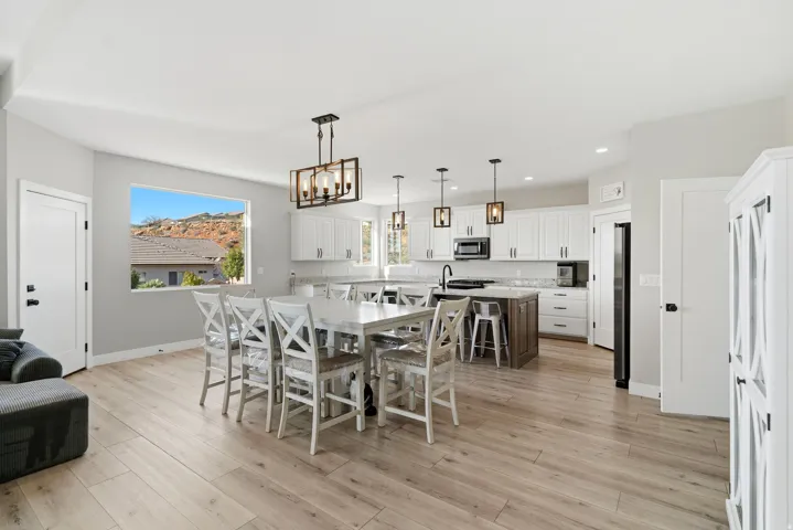 Open-concept living space featuring wood-finish flooring, a contemporary kitchen with white cabinetry and a contrasting island, and a dining area illuminated by a modern chandelier