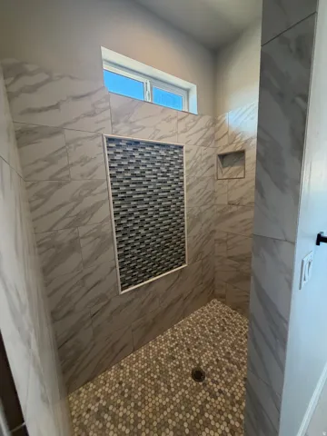 Walk-in shower featuring large format tiled walls with a mosaic accent, a tiled niche, and a pebble-style floor