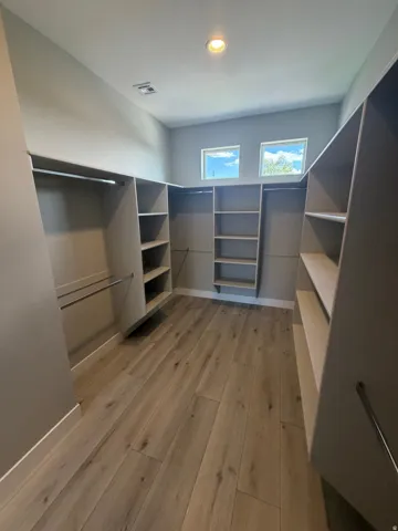 Spacious walk-in closet featuring extensive built-in shelving, hanging rods, and wood-finish flooring